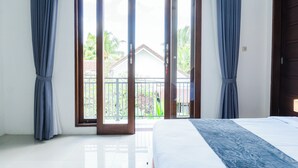 Une chambre avec un lit, une porte-fenêtre coulissante donnant sur un balcon et une vue sur une maison et la verdure environnante.