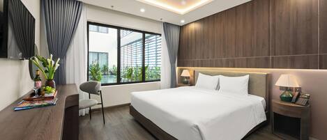 A modern hotel room with a large bed, a desk with a chair, a TV, and a window with curtains.