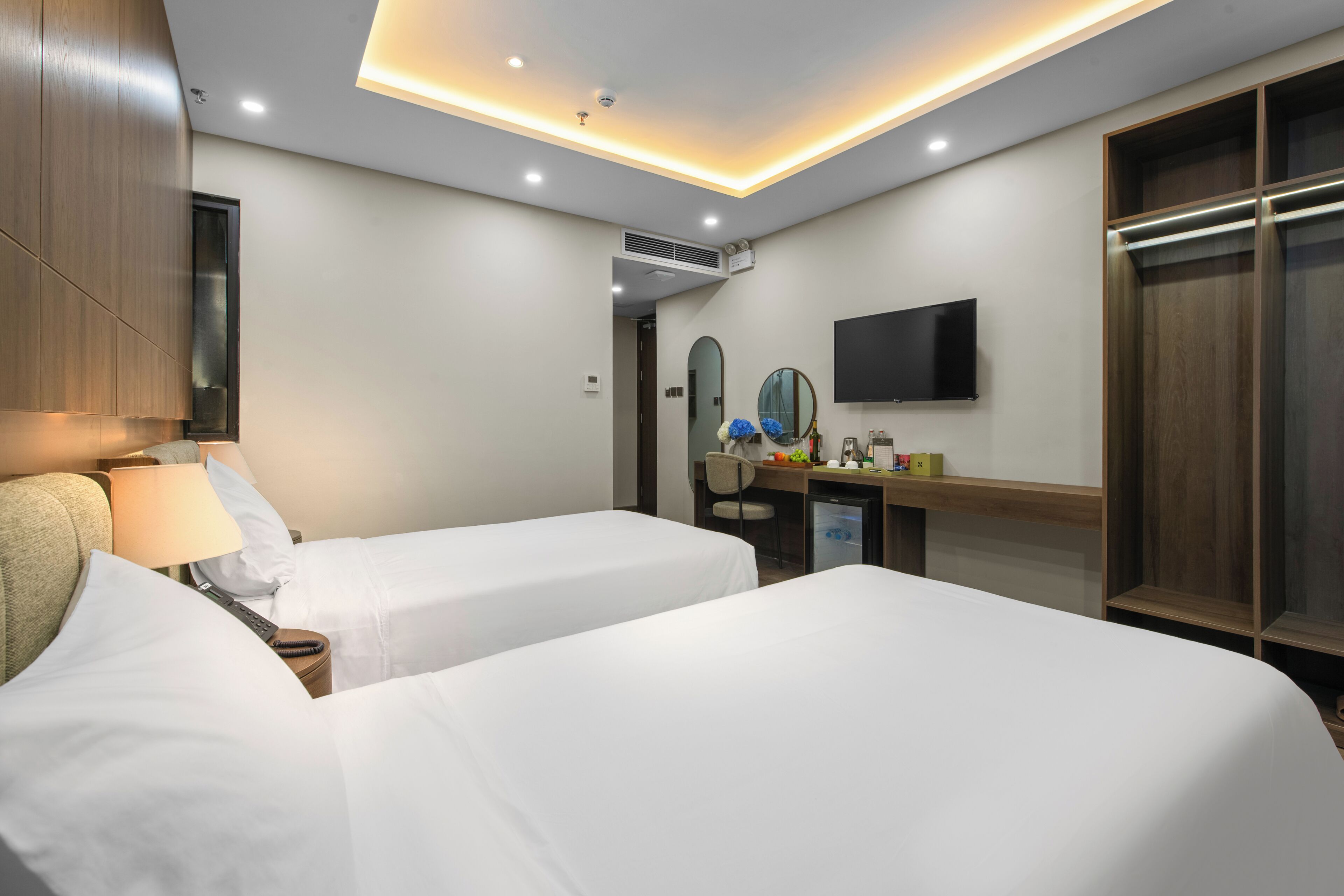 A hotel room with two beds, a desk with a chair, a television, and a wardrobe.