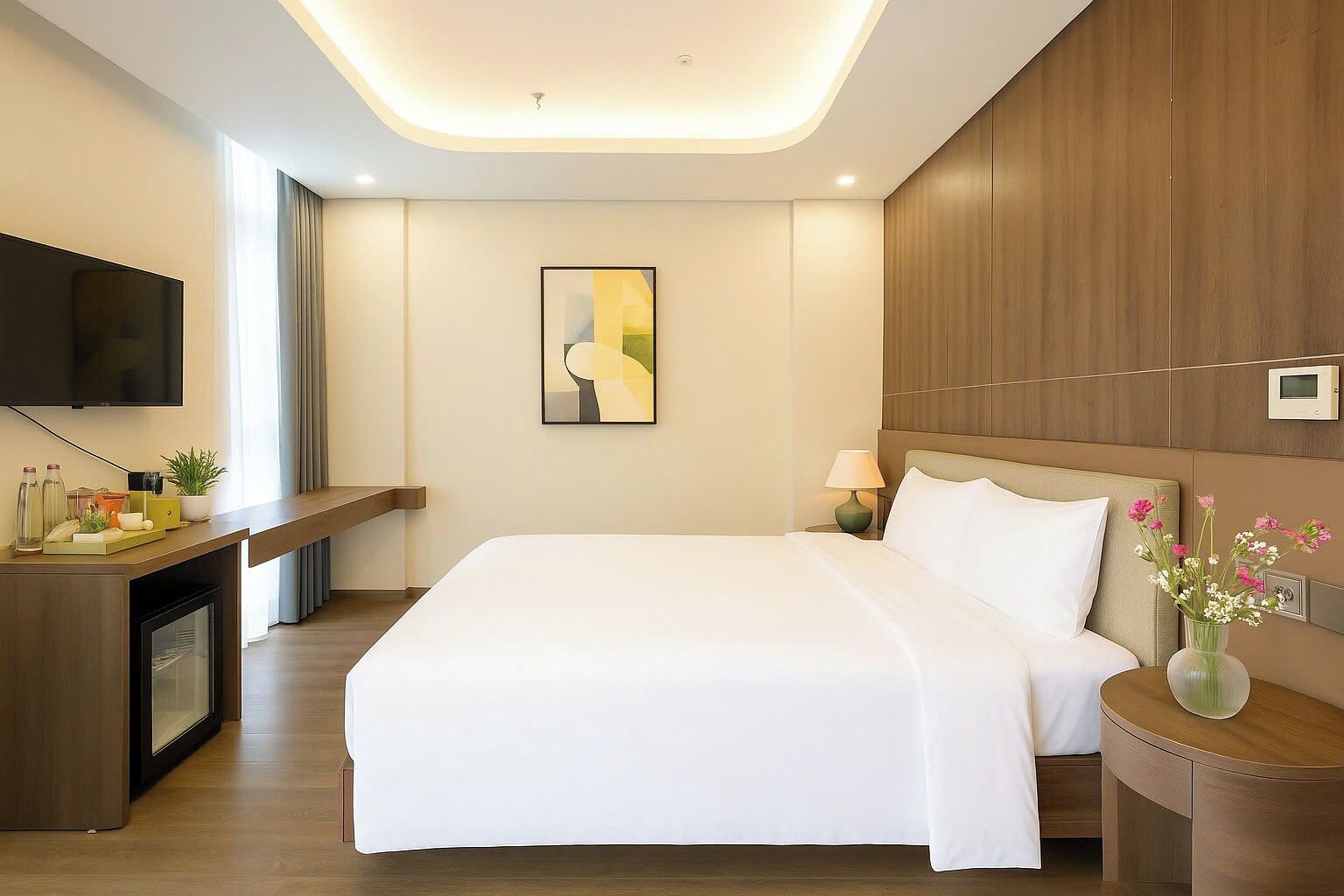 Une chambre d’hôtel moderne dotée d’un grand lit, d’un téléviseur à écran plat, d’un bureau avec un ordinateur et d’une petite table sur laquelle est posé un vase de fleurs.