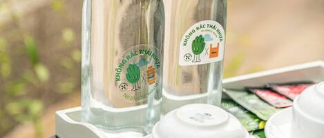 Two glass bottles with labels on a tray with white cups and saucers.