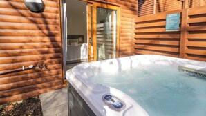 A hot tub in front of a wooden cabin with a glass door leading to a bedroom. - Luxury Lodge 44 (Rhyl)