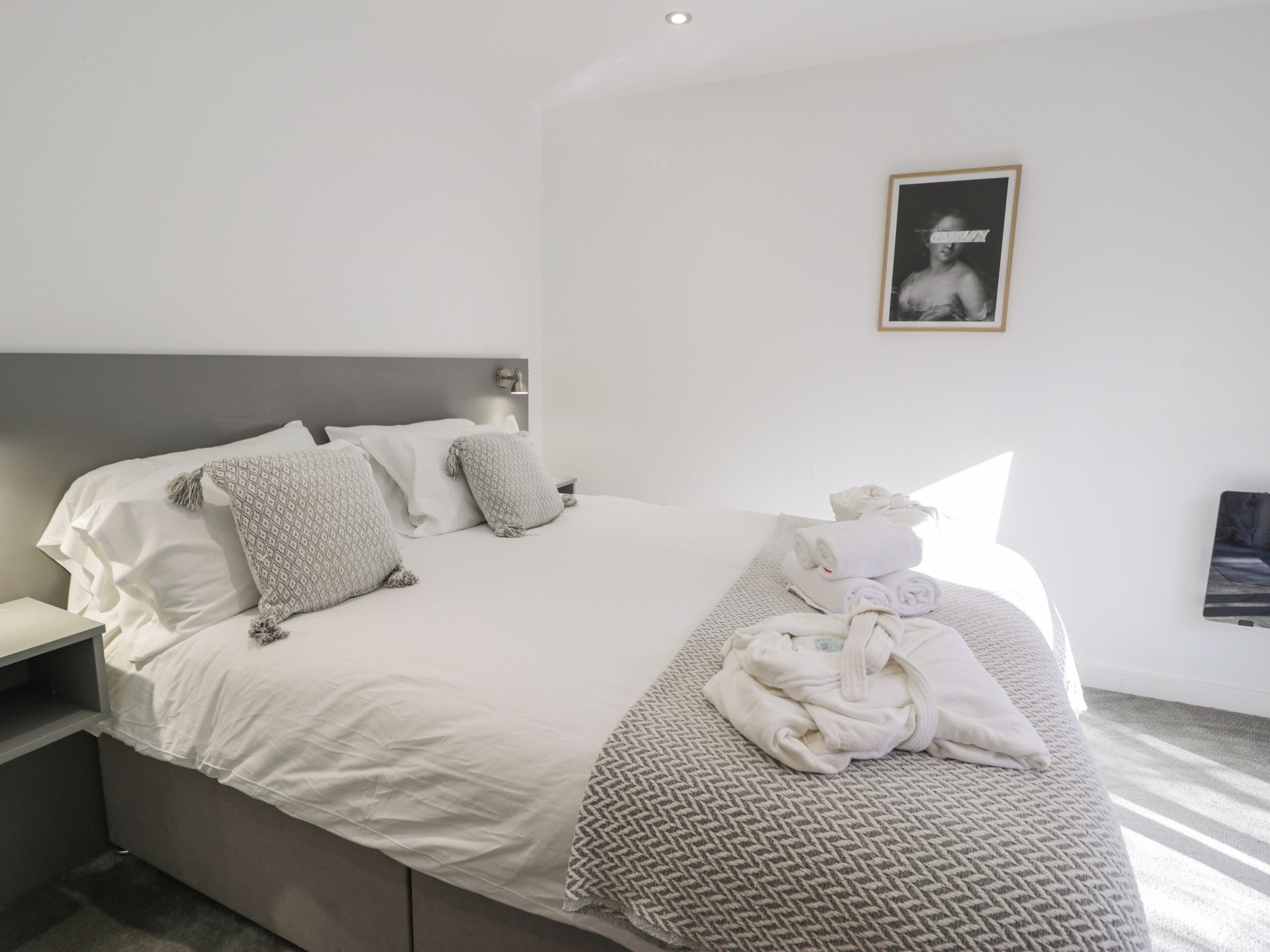 A neatly made bed with white linens and patterned pillows, a bedside table with a lamp, and a framed picture on the wall.