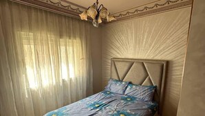 Un dormitorio con cama, candelabro y ventana con cortinas translúcidas.