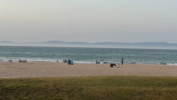 Una playa con gente, sillas y algunos contenedores de basura.