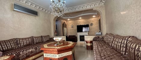 A spacious living room with patterned sofas, a central coffee table, and a chandelier.