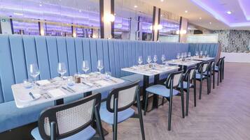 A restaurant with blue booths and tables, each set with cutlery and wine glasses.