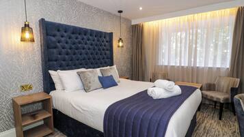 A hotel room with a large bed, a wooden nightstand, a chair, and a window with curtains.