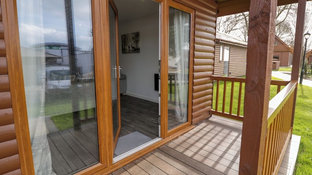 A wooden cabin with a sliding glass door leading to a covered porch. - Premier Lodge 78 (Rhyl)