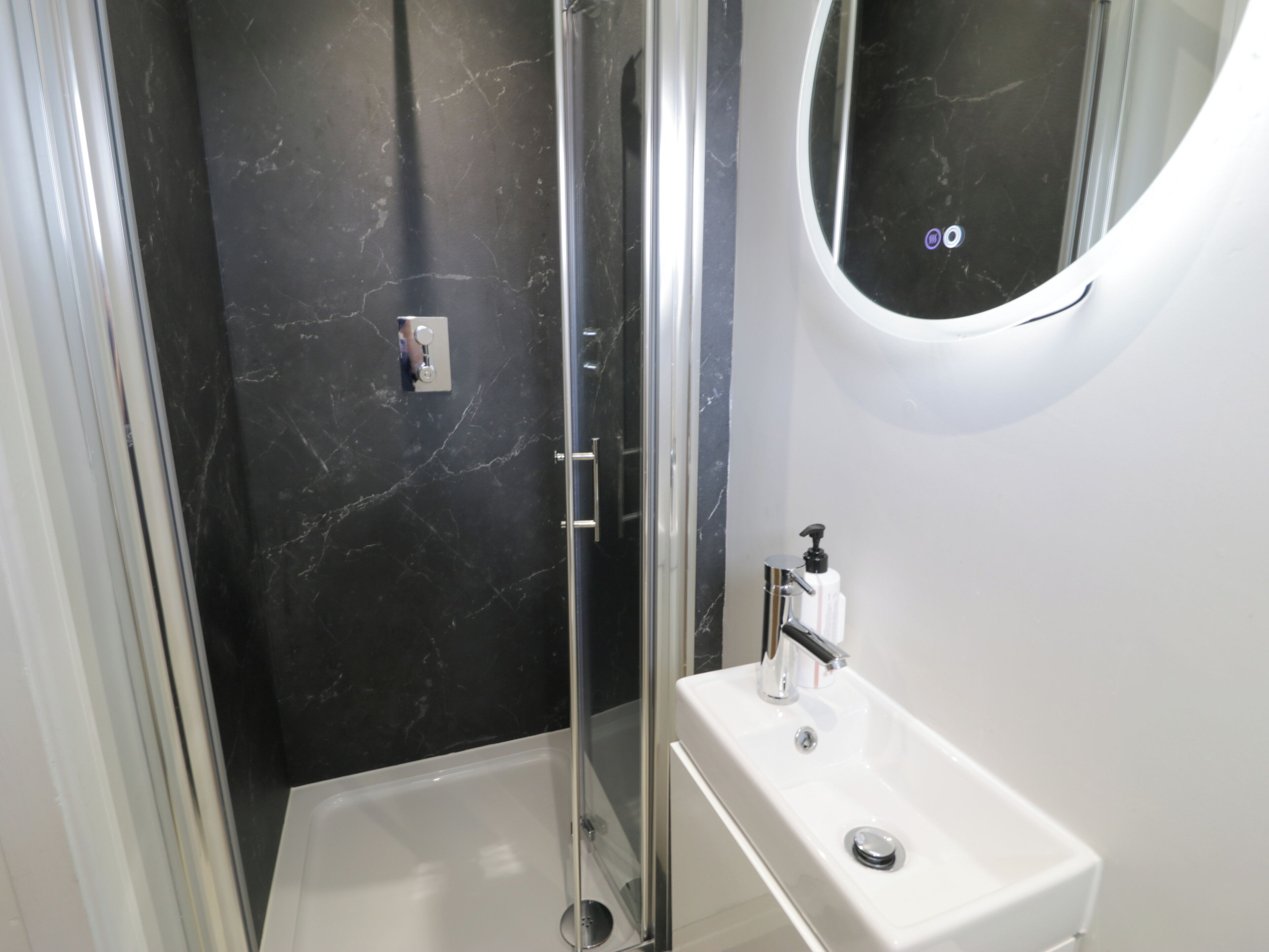 Un baño con ducha envuelta en vidrio, un lavabo blanco y una pared de mármol.