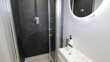 Un baño con ducha envuelta en vidrio, un lavabo blanco y una pared de mármol.