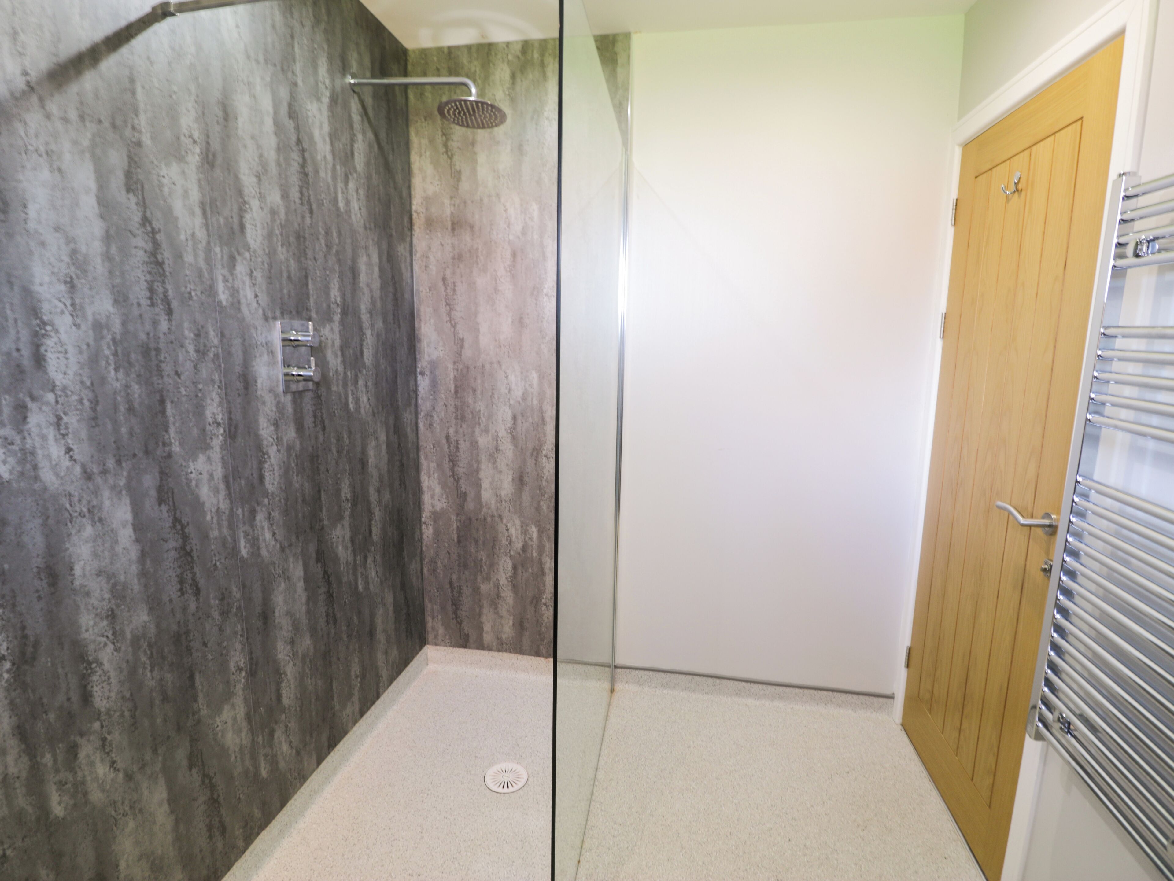 A shower with a glass door, a wooden door, and a metal towel rack.