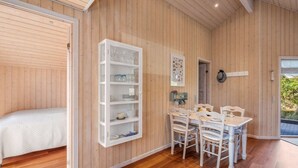 Un intérieur en bois comprenant un coin repas, une étagère blanche et un lit.