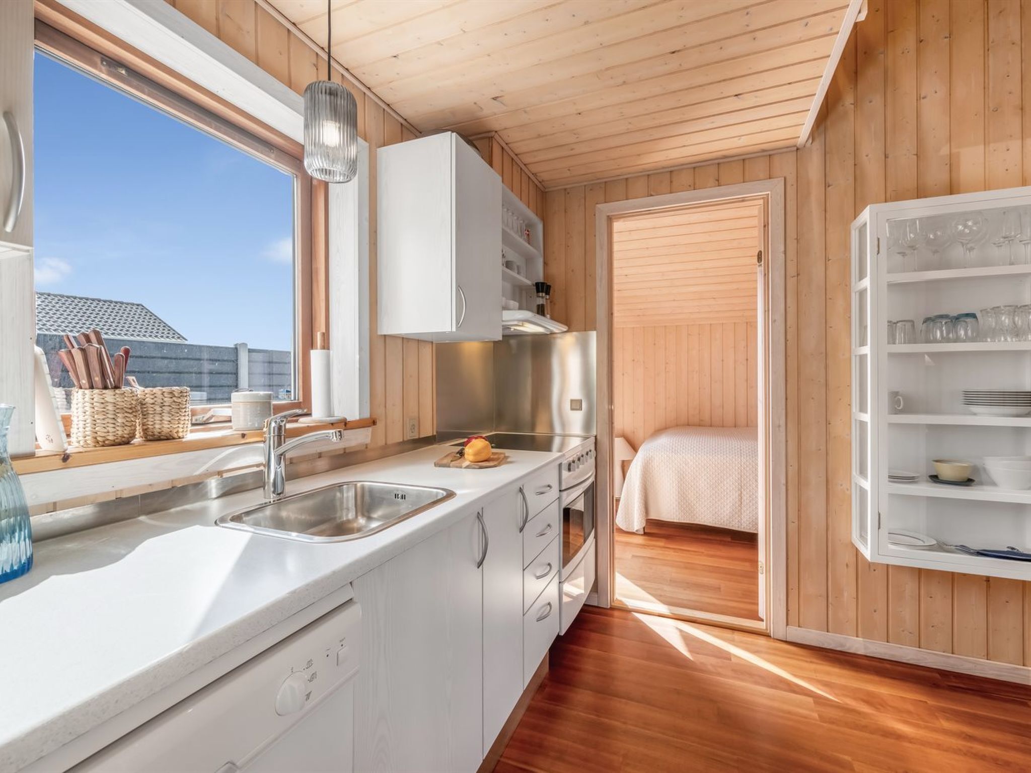 A compact kitchen with a sink, stove, and cabinets, a small dining area with a table and chairs, and a bed in a separate room.