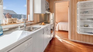 Une cuisine compacte comprenant un évier, une cuisinière et des placards, un petit coin repas avec une table et des chaises, et un lit dans une pièce séparée.