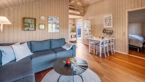 Un salon chaleureux avec un canapé bleu, une table basse ronde ornée de fruits, des murs en bois et un coin repas avec des chaises blanches.