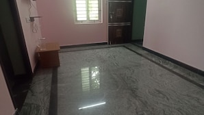 Una habitación amplia con suelo de mármol, una ventana con persianas, una puerta y una pequeña mesa de madera.