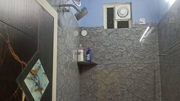 A bathroom with a shower, toilet, and a small shelf with toiletries.