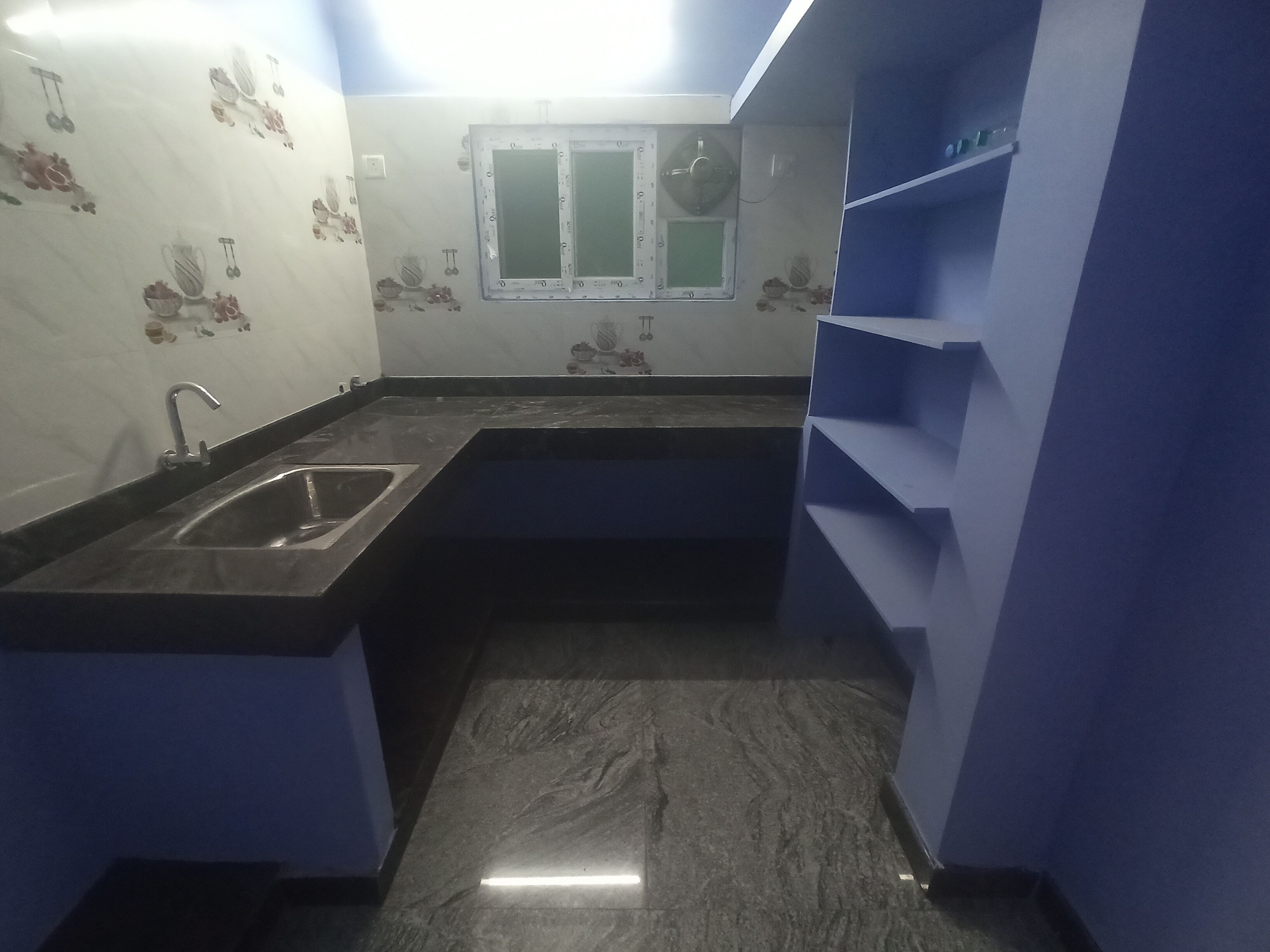 A compact kitchen with a sink, a window, and blue shelving.