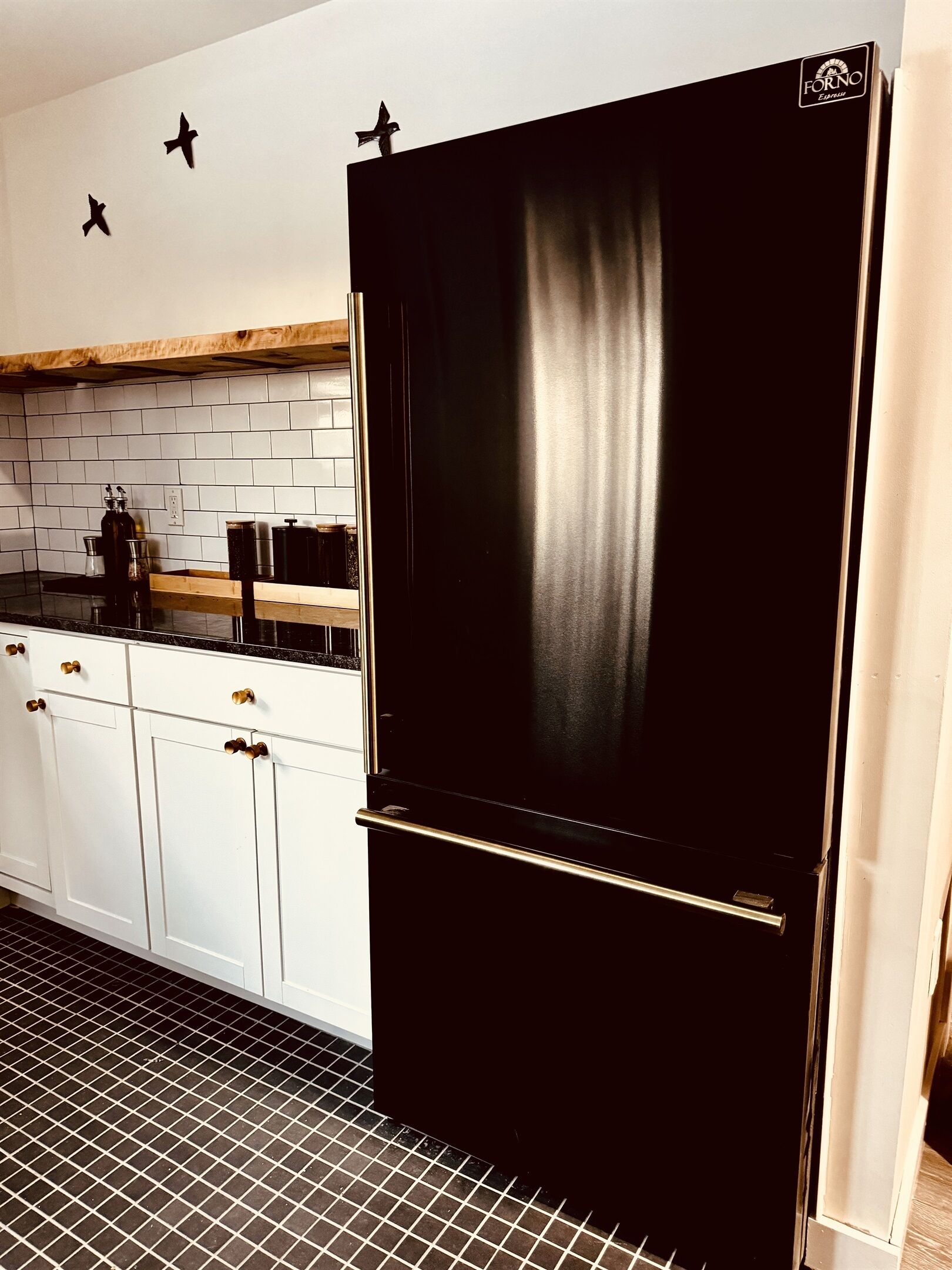 Eine Küche mit einem schwarzen Kühlschrank, weißen Schränken und einer gefliesten Spritzschutzwand.