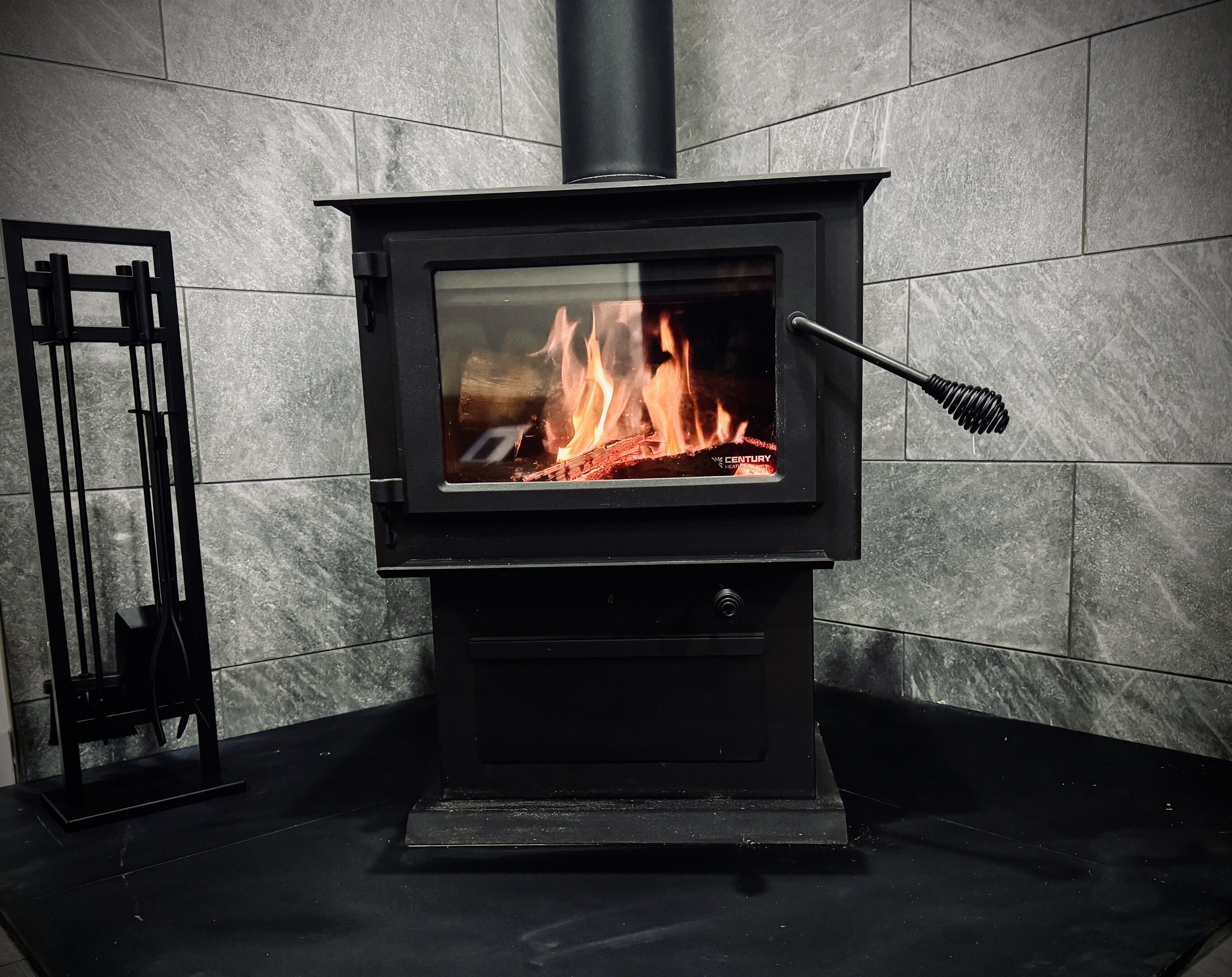 A black wood-burning stove with a glass front, a chimney, and a metal fire screen.