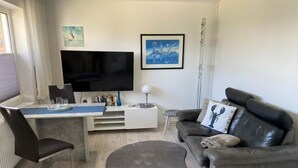 A modern living room with a flat-screen TV, a sofa, a coffee table, and a dining area with chairs and a table.