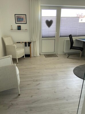 Une piĂšce comprenant une chaise en osier blanche, un fauteuil de bureau noir, une petite table et une fenĂȘtre avec un store en forme de cĆur.
