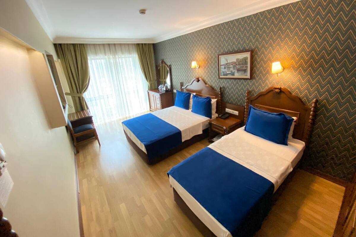 A hotel room with two beds, wooden headboards, a mirror, a nightstand, a dresser, and a window with curtains.