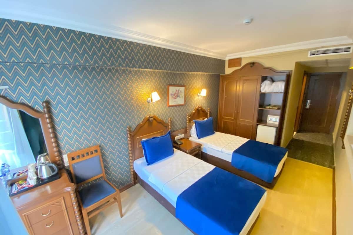 A hotel room with two beds, a wooden wardrobe, a desk with a chair, and a mirror.