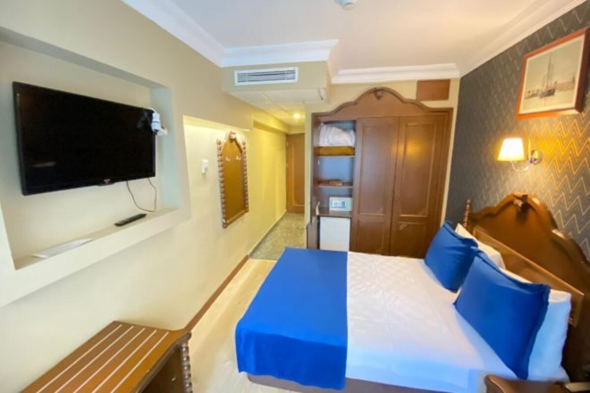 A hotel room with a bed, a TV mounted on the wall, a wardrobe, and a small table.