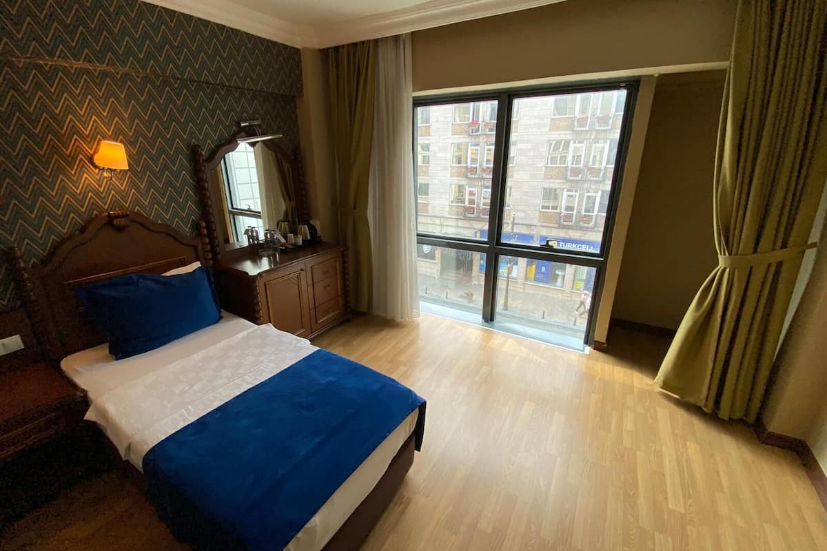A hotel room with a bed, a dresser, a mirror, and a view of the city through large windows.