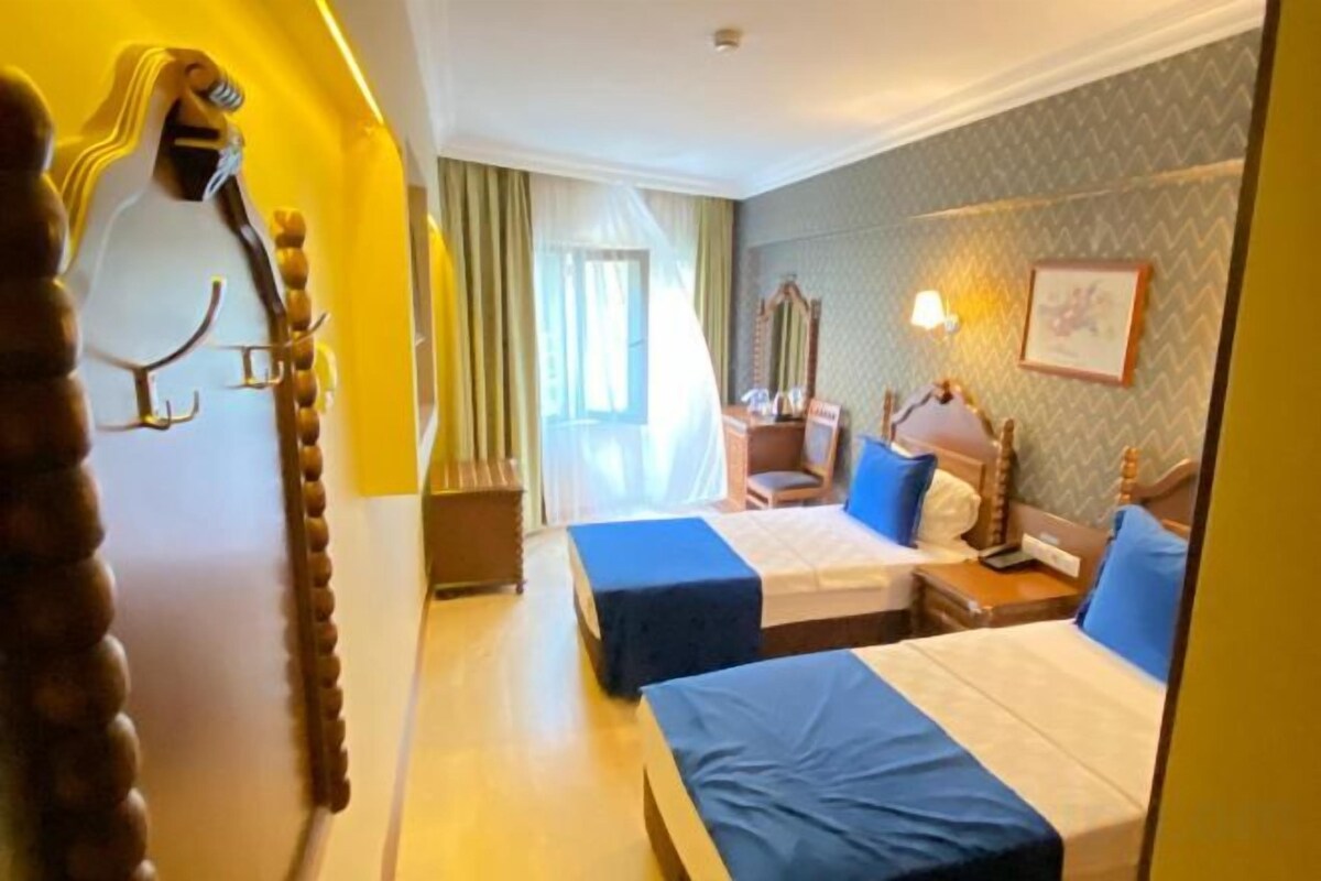 A hotel room with two beds, a desk, a chair, and a mirror.