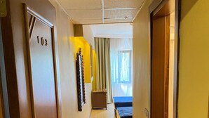 Pasillo de hotel con suelo de mármol, una cama y un baño a lo lejos.