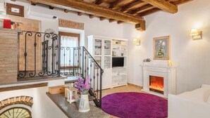 Een woonkamer met een open haard, een trap met smeedijzeren leuning en een witte boekenkast.