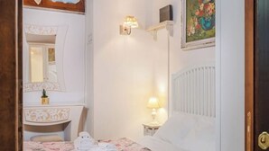 Een hotelkamer met een bed, nachtkastje met een lamp, een spiegel en een bloemenbedekking.