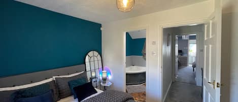 Quarto com cama, mesa de cabeceira, espelho e luminária no teto.