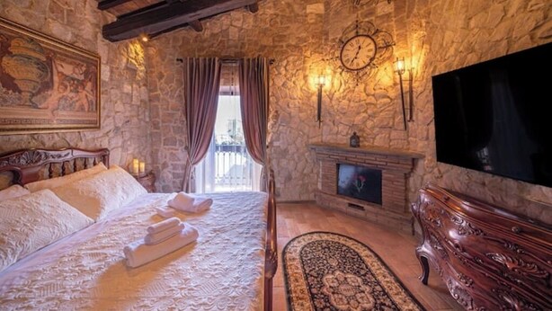 Une pièce avec un mur en pierre, un lit avec du linge de maison blanc, une cheminée et un téléviseur.
