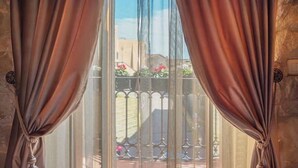 Une fenêtre ornée de rideaux légers, donnant sur un balcon avec une balustrade en métal et des plantes en pot.
