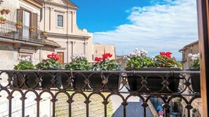 Un bâtiment à la façade classique, un balcon orné de plantes en pot et un ciel d’un bleu limpide.