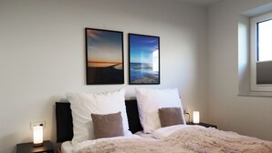 Un dormitorio con una cama, dos mesitas de noche, dos cuadros en la pared y una ventana.