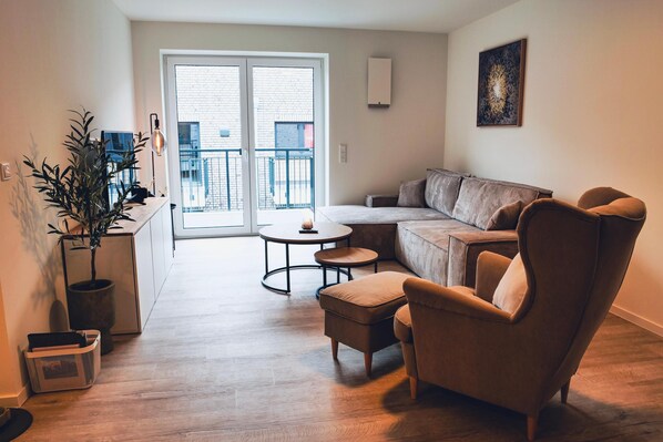 Un salon moderne avec un canapé d’angle, une table basse ronde et une plante en pot.