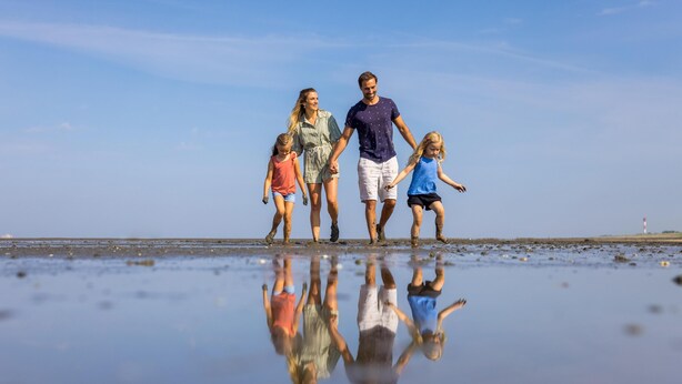 Una familia caminando sobre una playa mojada, con sus reflejos visibles en el agua.