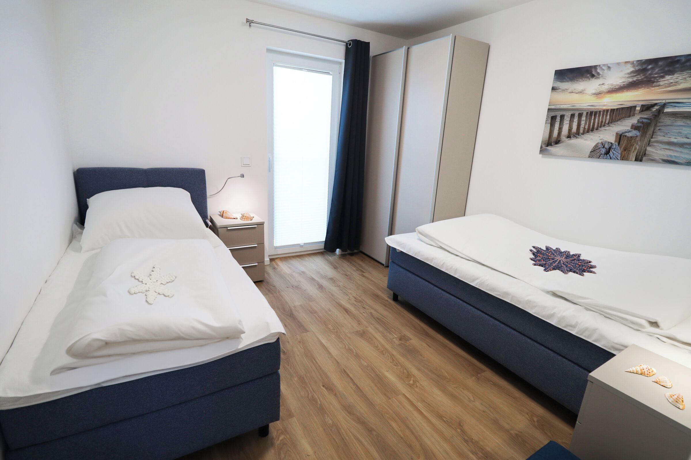 Un dormitorio con dos camas, una mesita de noche, una ventana con cortinas y un cuadro en la pared.
