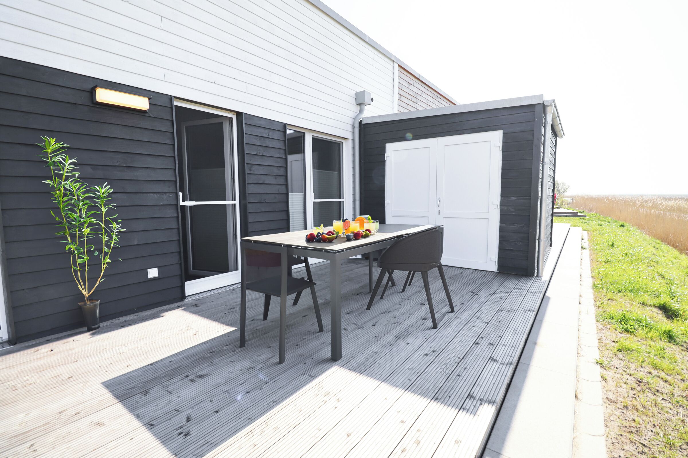 An outdoor patio with a table and chairs, a potted plant, and a building with a dark exterior and white garage doors.