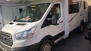 A white RV with a 'For Sale' sign on the windshield, parked next to a building with a brick facade. - ford zefiro 675 6 berth (wigan)