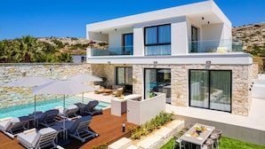 Una casa moderna de dos pisos con piscina, mobiliario exterior y un muro de piedra.