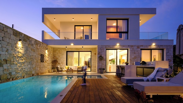 Una casa moderna de dos pisos con piscina, mobiliario exterior y un muro de piedra.
