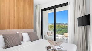 Habitación de hotel moderna con una cama grande, un panel de pared de madera, un balcón con vistas y un televisor de pantalla plana.