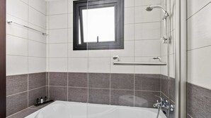 A modern bathroom with a bathtub, a shower, and a window. - Aether Residence by Nomads (Larnaca)