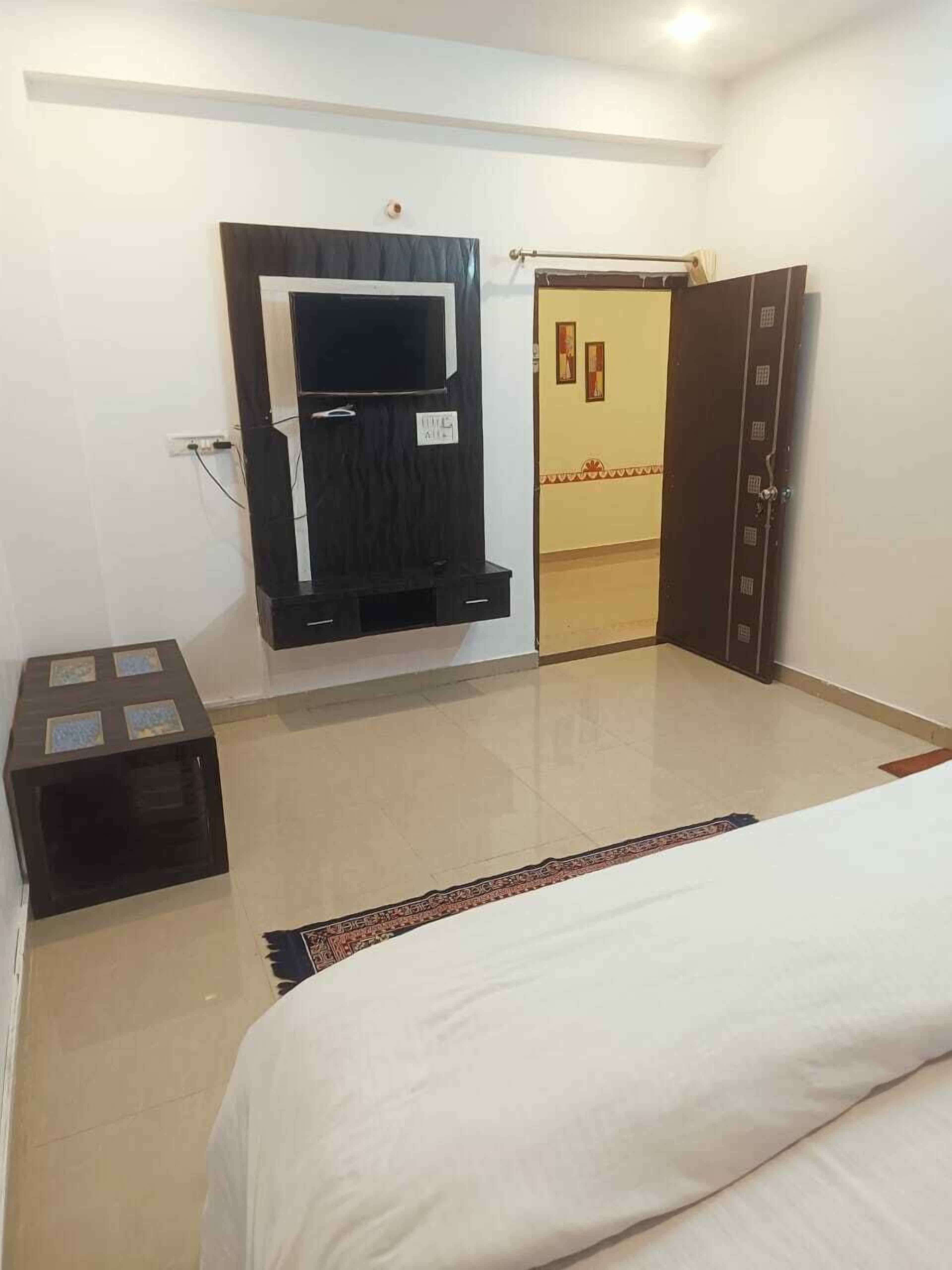A bedroom with a bed, a wardrobe, a TV mounted on the wall, and a small table.